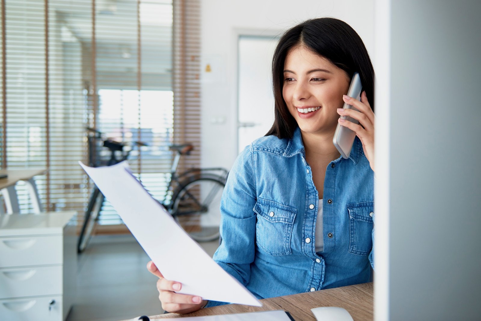 Cheerful Asian woman in the office talking on the phone