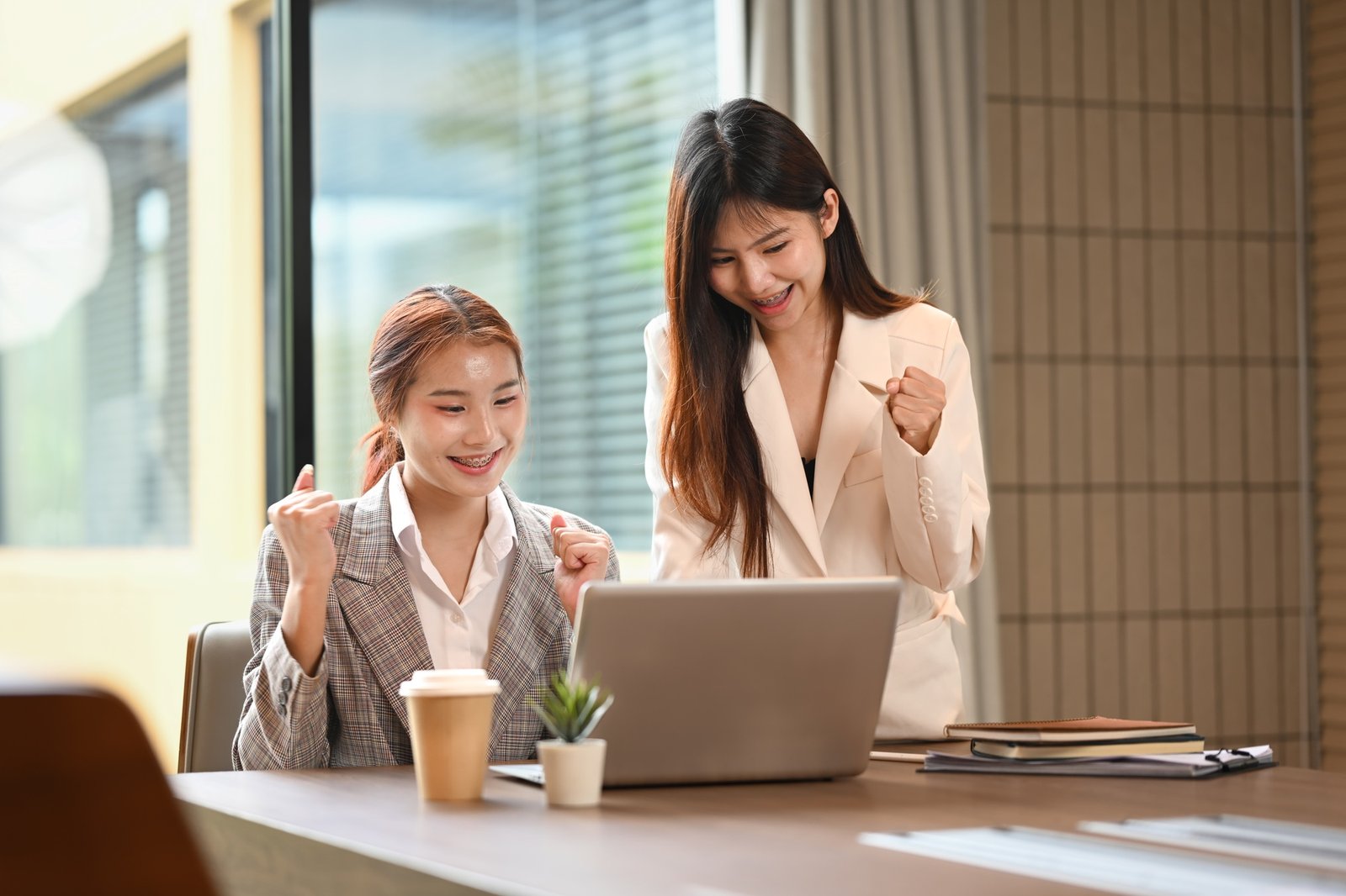 Happy young business women looking at laptop celebrating business success in the office